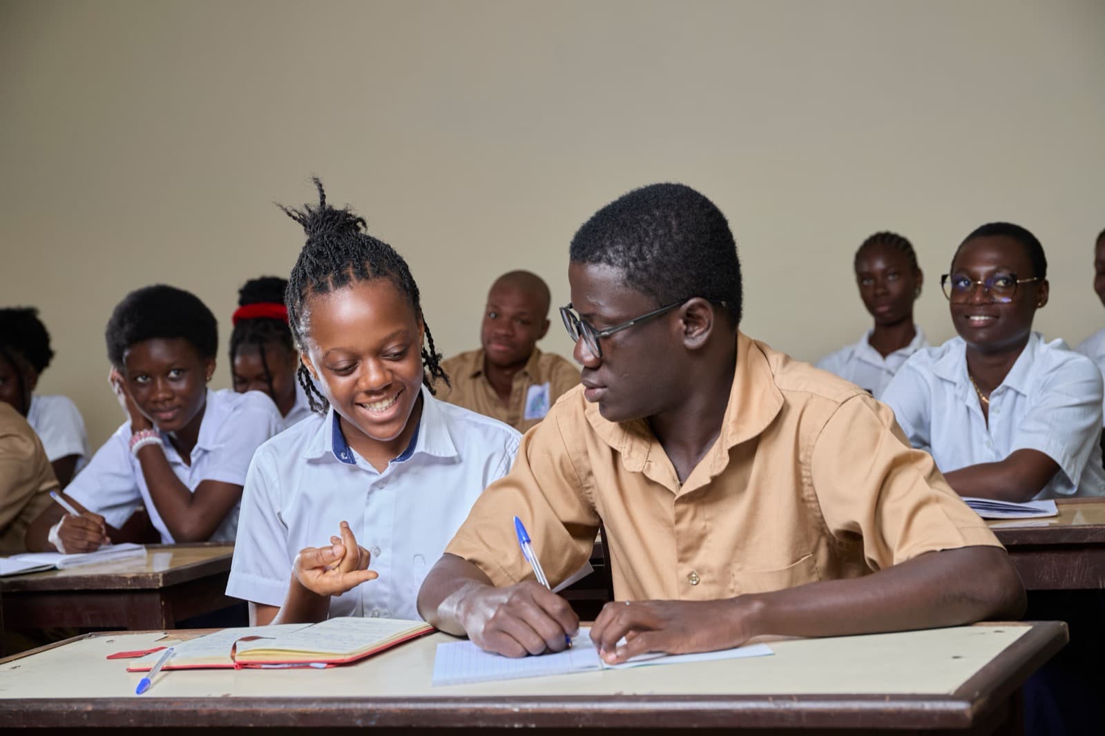 Students writing together at a desk in class.